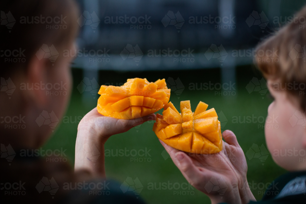 kids holding up sliced mango as they're eating it - Australian Stock Image