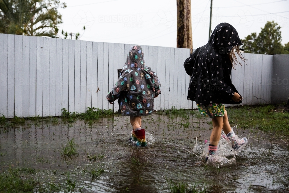 kids in gumboots and raincoats splashing in puddles - Australian Stock Image
