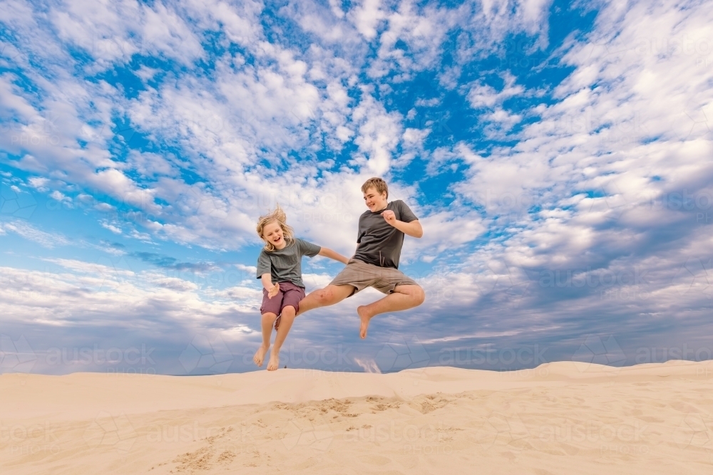 Kids jumping for joy on the sand dunes of Stockton Beach at Port Stephens - Australian Stock Image