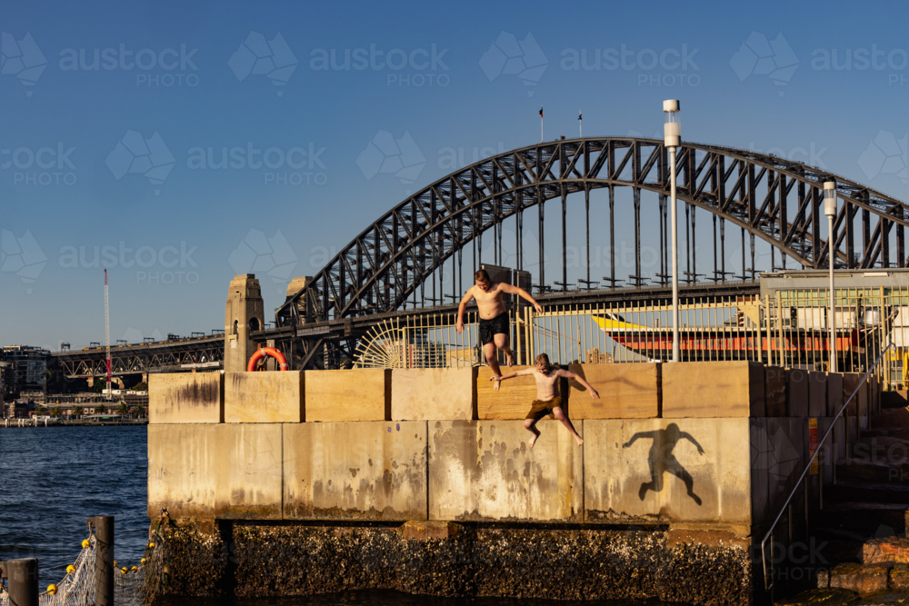 Kids jumping from ledge into water with Sydney Harbour Bridge in the background - Australian Stock Image