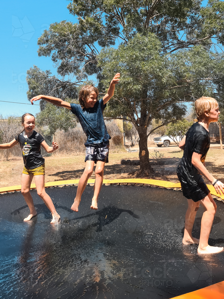 Kids jumping on trampoline in Aussie backyard in the summer - Australian Stock Image