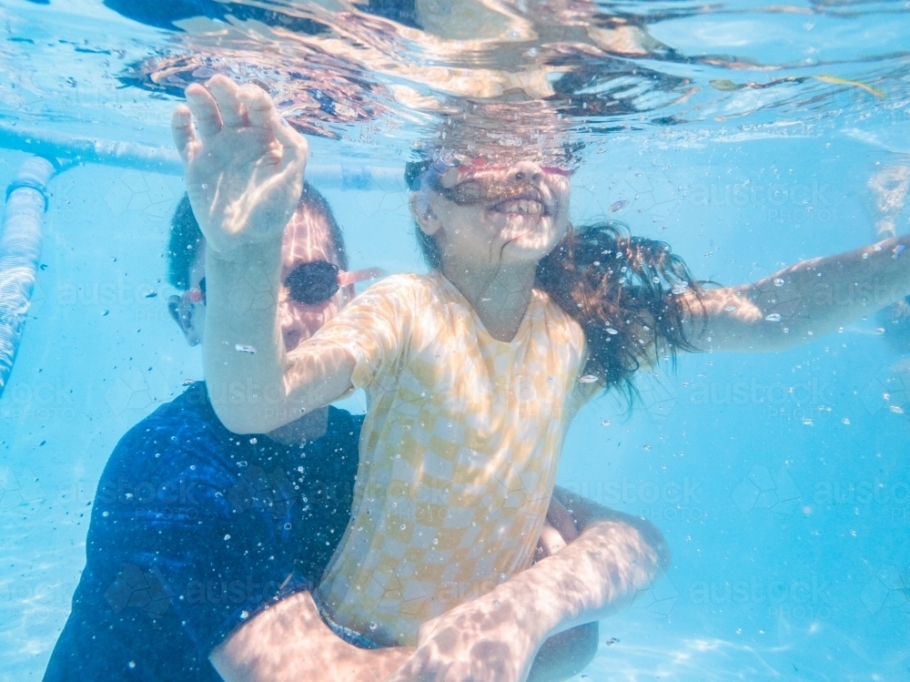 Image of Kids playing in pool holding each other under water while