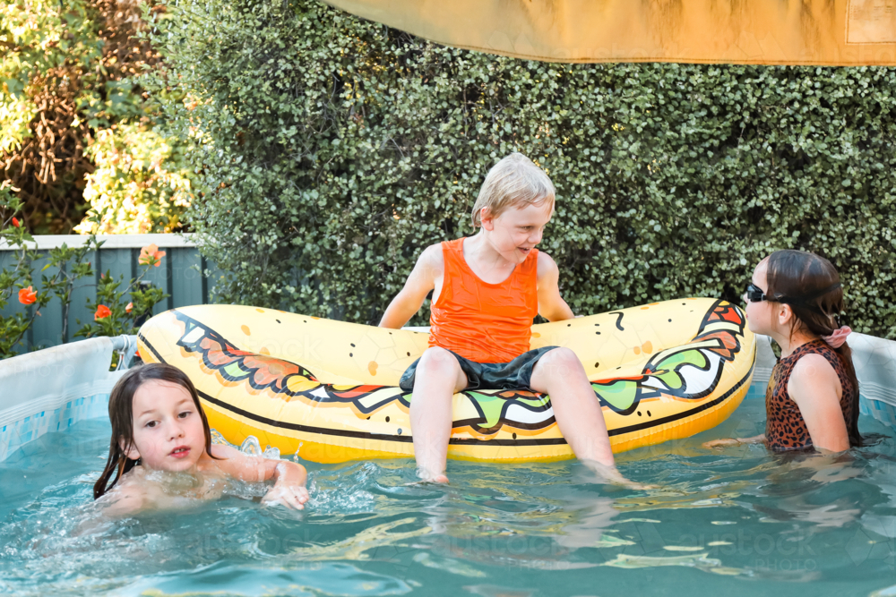 Kids playing with inflatable taco in backyard swimming pool - Australian Stock Image