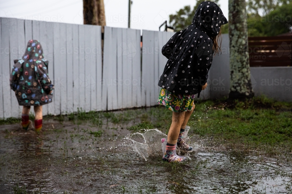 kids splashing in puddles in the front yard on a rainy day - Australian Stock Image