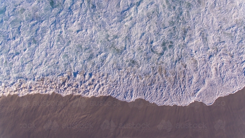 Lacy pattern of water as waves rush over the sand on the beach : Austockphoto Lacy pattern of water as waves rush over the sand on the beach - Australian Stock Image