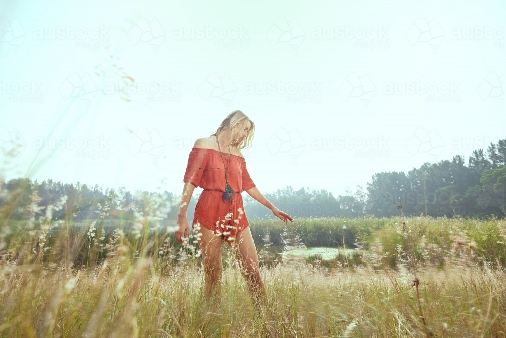 Lady in red walking in a field of grass - Australian Stock Image