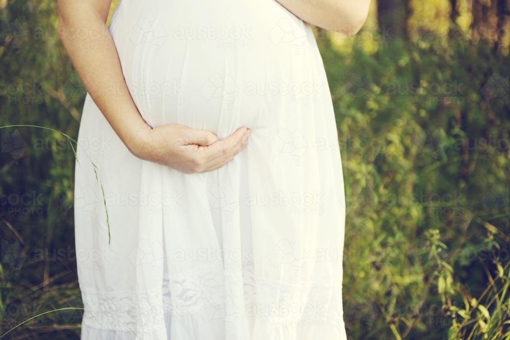 lady in white dress holding her pregnant belly - Australian Stock Image