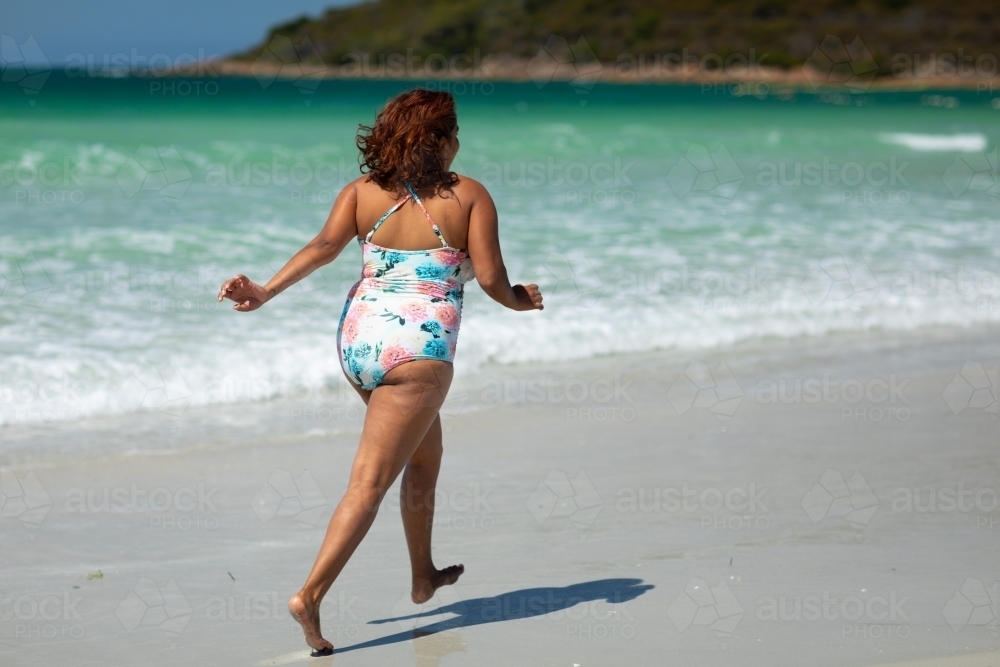 lady running along sea shore wearing swimming costume - Australian Stock Image