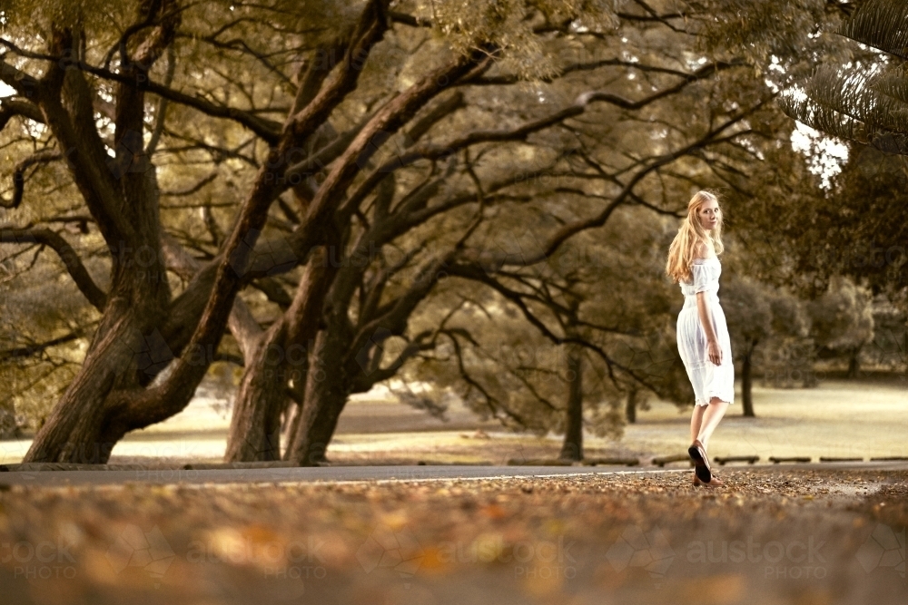 Lady walking amongst the trees in a white dress during autumn - Australian Stock Image