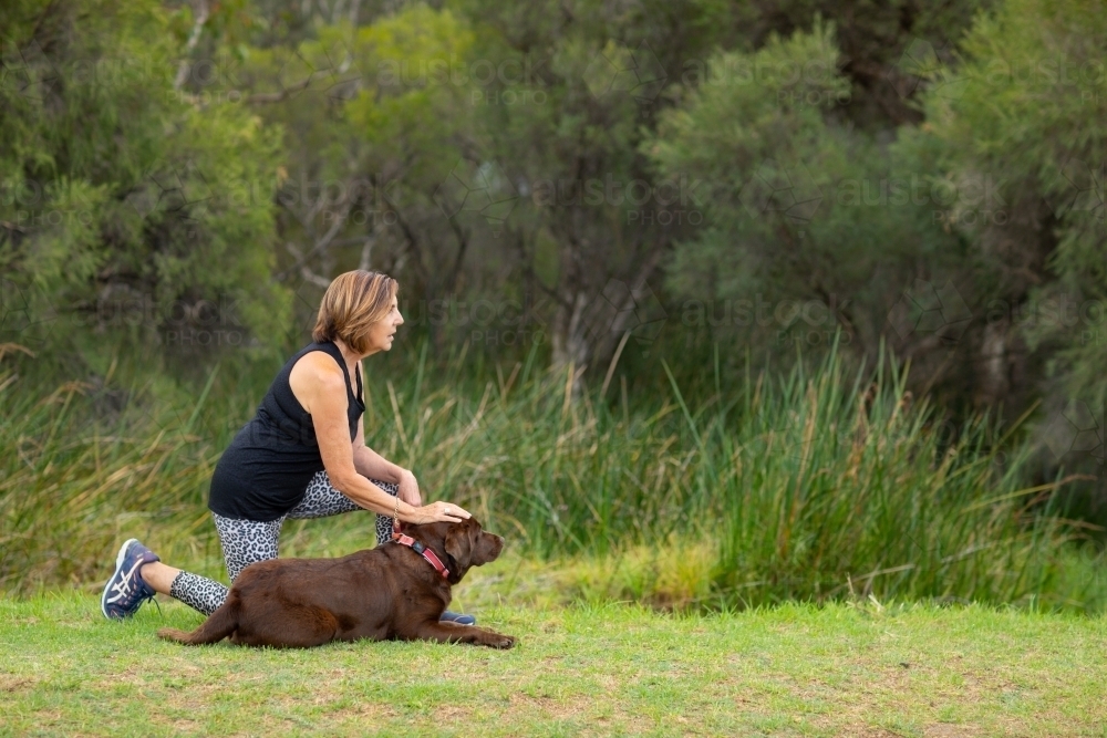 lady with chocolate Labrador lying down in green parkland - Australian Stock Image