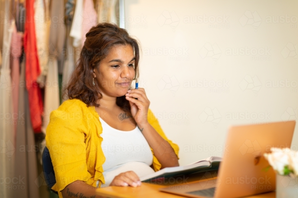 lady with hand touching chin in home office with book and computer - Australian Stock Image