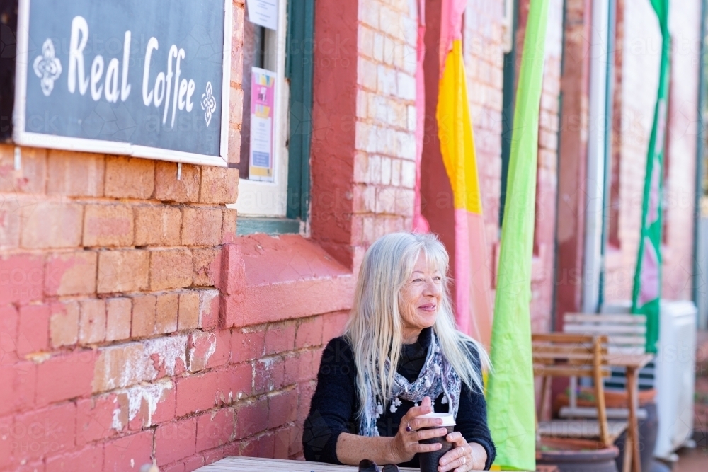 lady with takeaway coffee sitting outside coffee shop - Australian Stock Image