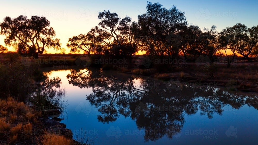Lake with silhouetted gum trees at sunset - Australian Stock Image