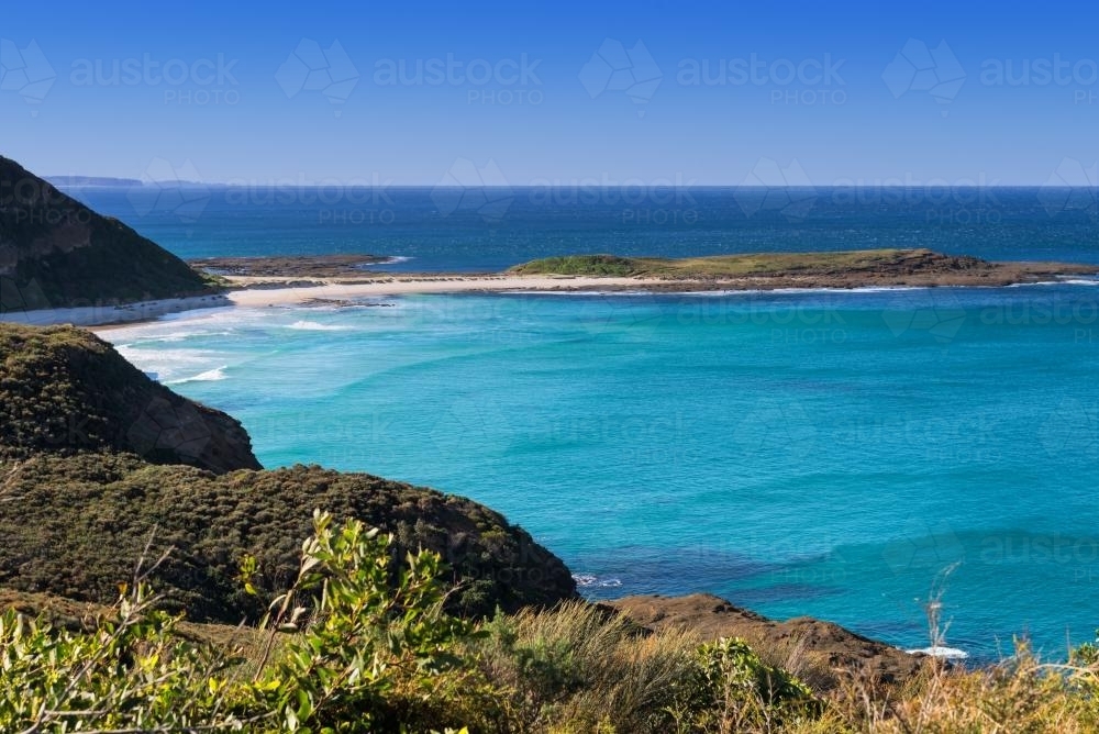 Landscape of beach and green headland beside clean blue water - Australian Stock Image