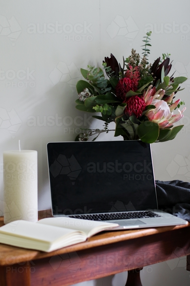 Laptop and notebook on a wooden desk with a bouquet of native flowers - Australian Stock Image