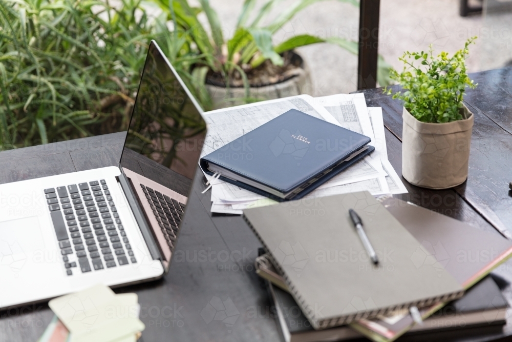 Laptop and planning documents on table outdoors - Australian Stock Image