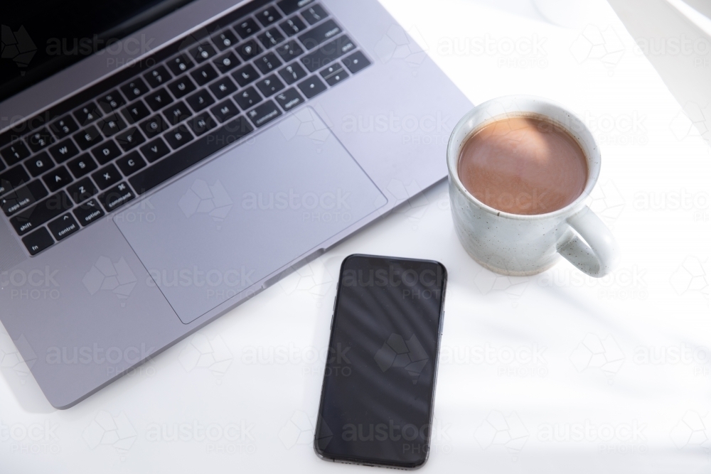 laptop and smart phone with blank screen and mug of hot beverage on a white desk - Australian Stock Image