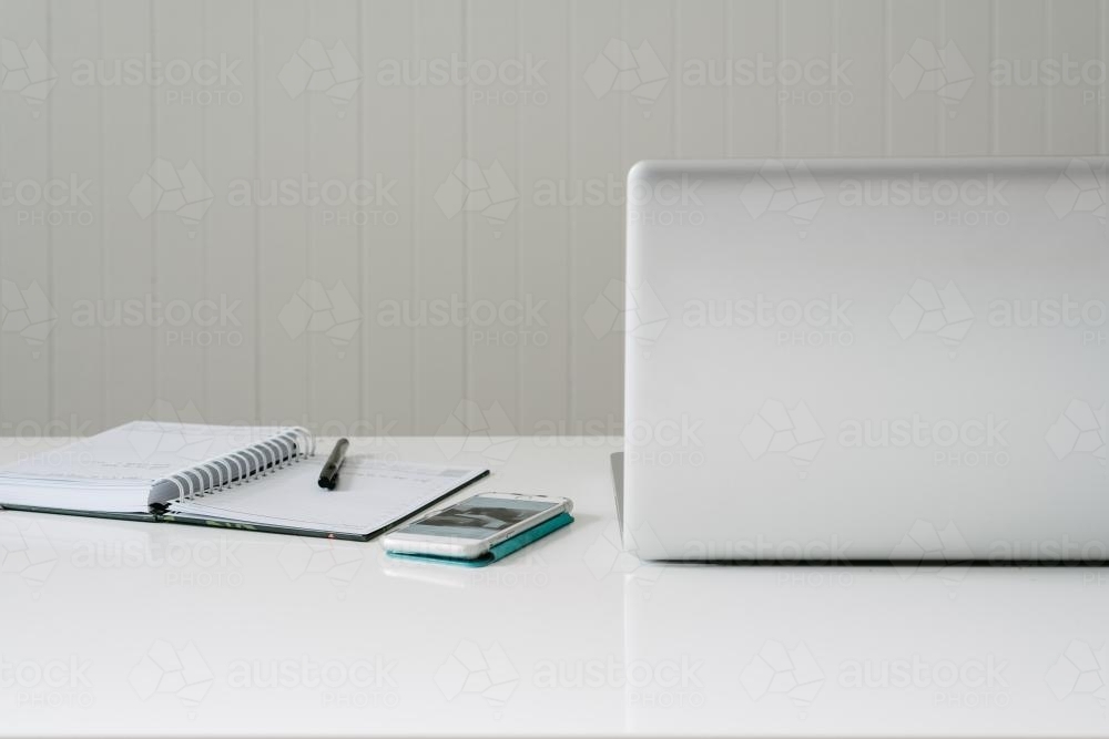 laptop, phone and diary on a white desk - Australian Stock Image