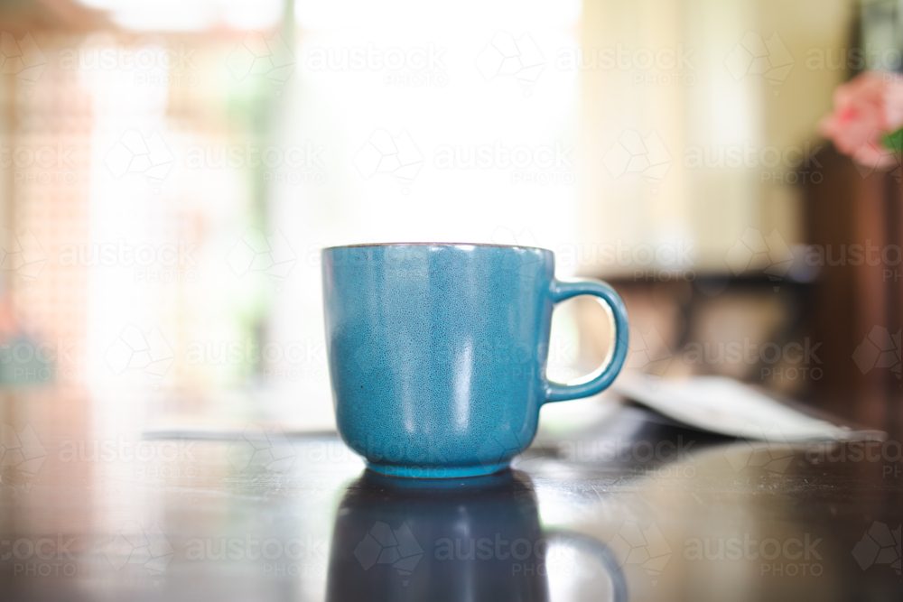 Large blue coffee mug on coffee table with brightly lit background - Australian Stock Image