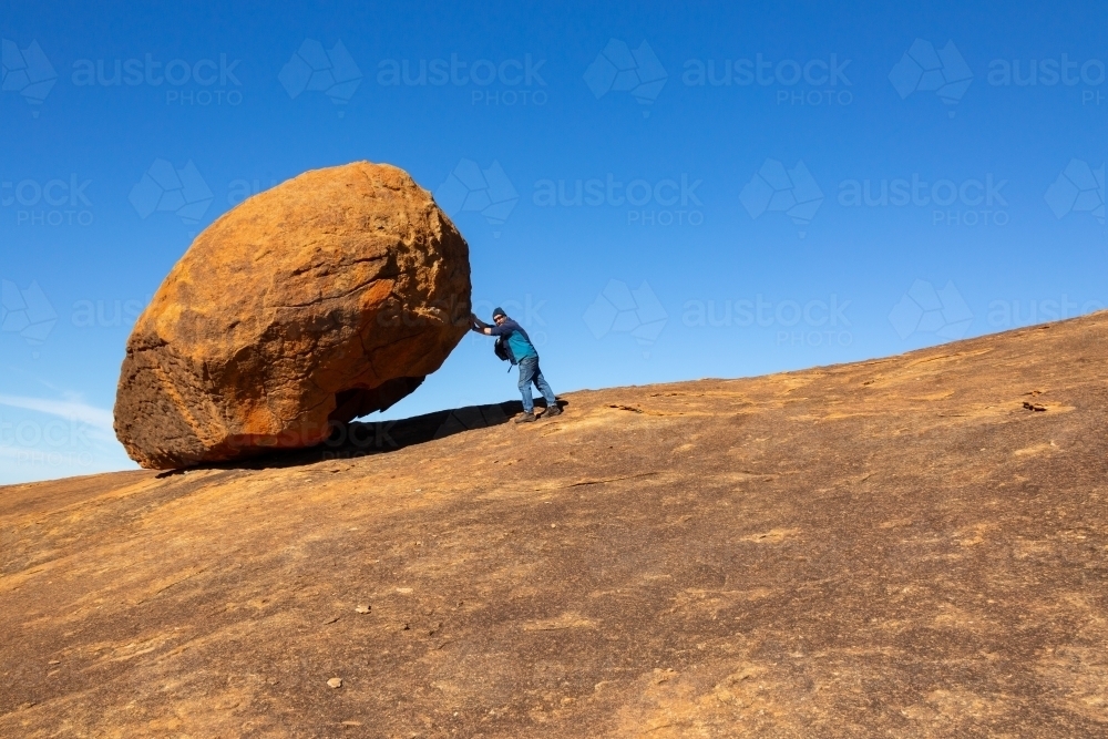 Large granite boulder dwarfs man pretending to push it - Australian Stock Image