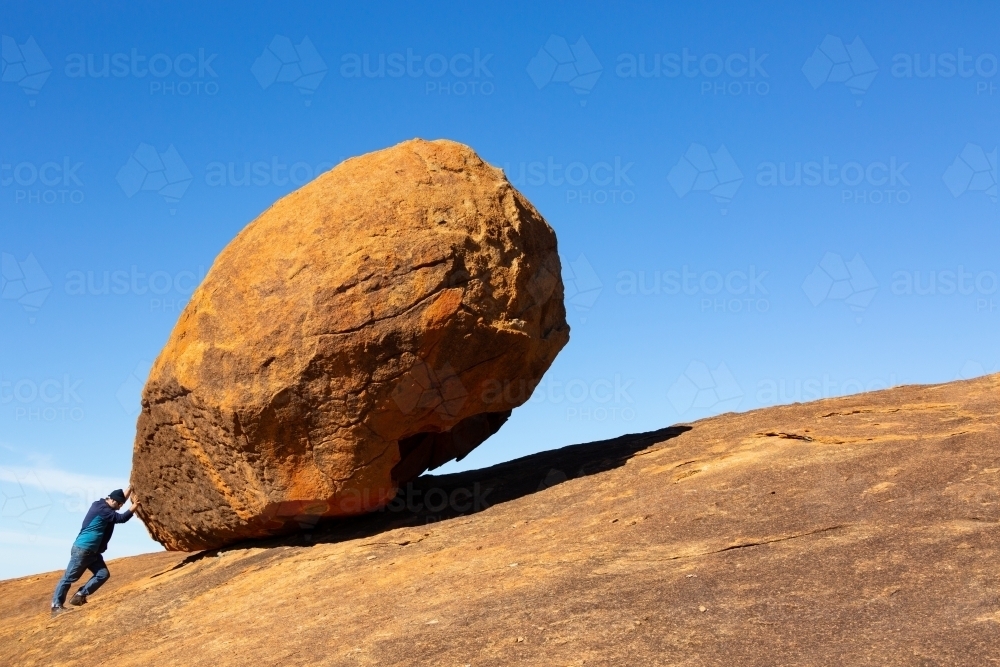 Large granite boulder dwarfs man pretending to push it - Australian Stock Image