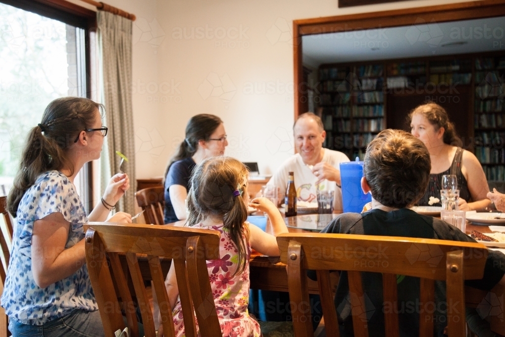 Large happy family having a meal together around the dining table inside - Australian Stock Image