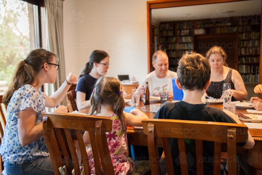Large happy family having a meal together around the dining table inside - Australian Stock Image