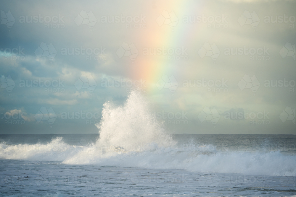 Large wave splashing into white spray with bright rainbow in background at Scarborough Beach, Perth - Australian Stock Image