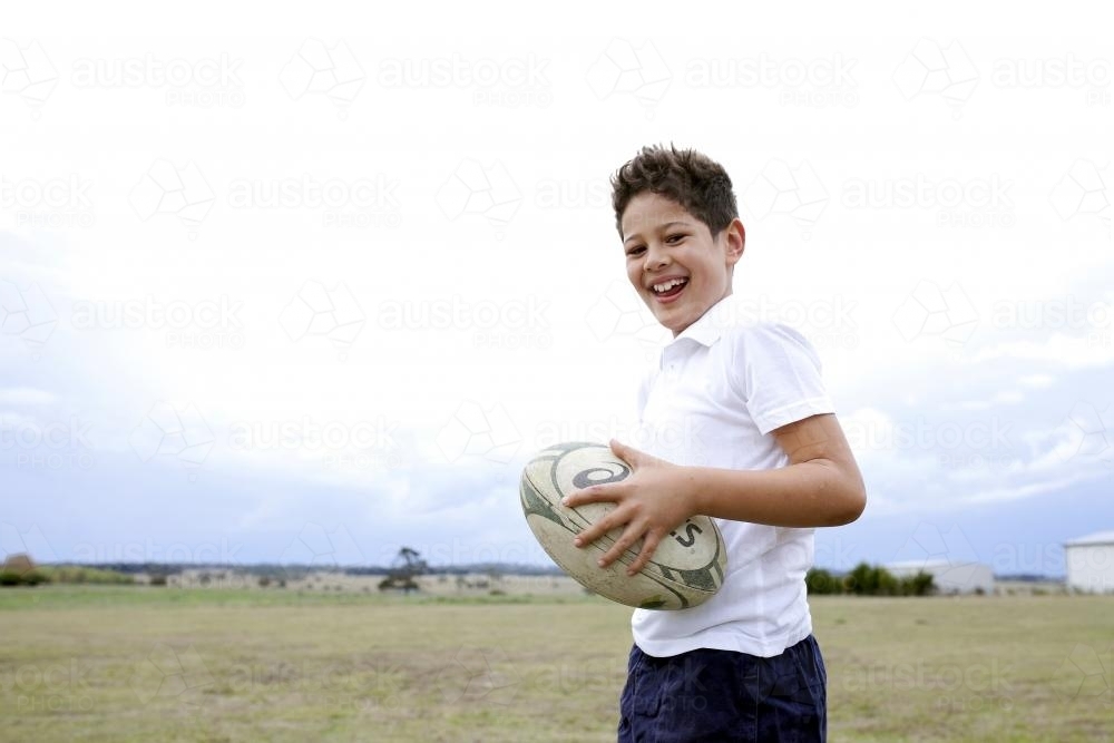 Laughing boy holding football outside - Australian Stock Image