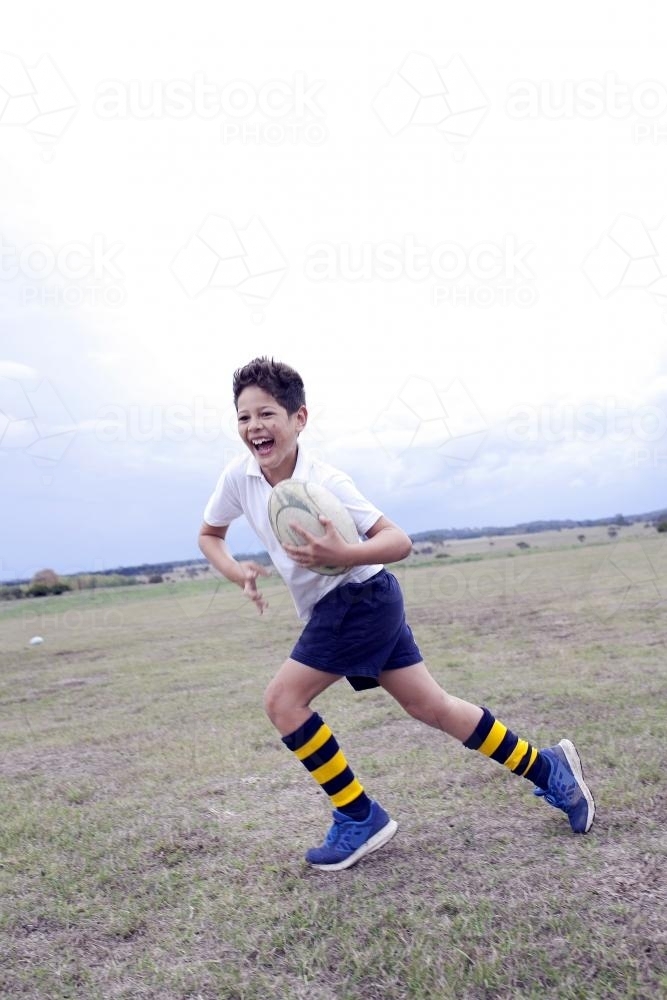 Laughing boy running with football in a field - Australian Stock Image