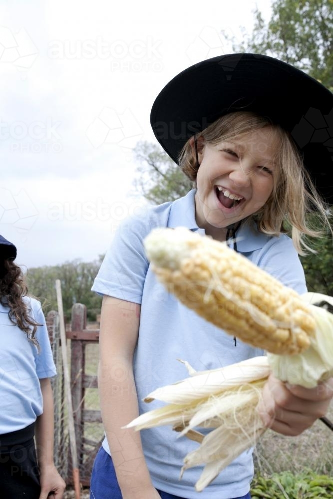 Laughing girl in school uniform holding freshly picked corn on the cob - Australian Stock Image