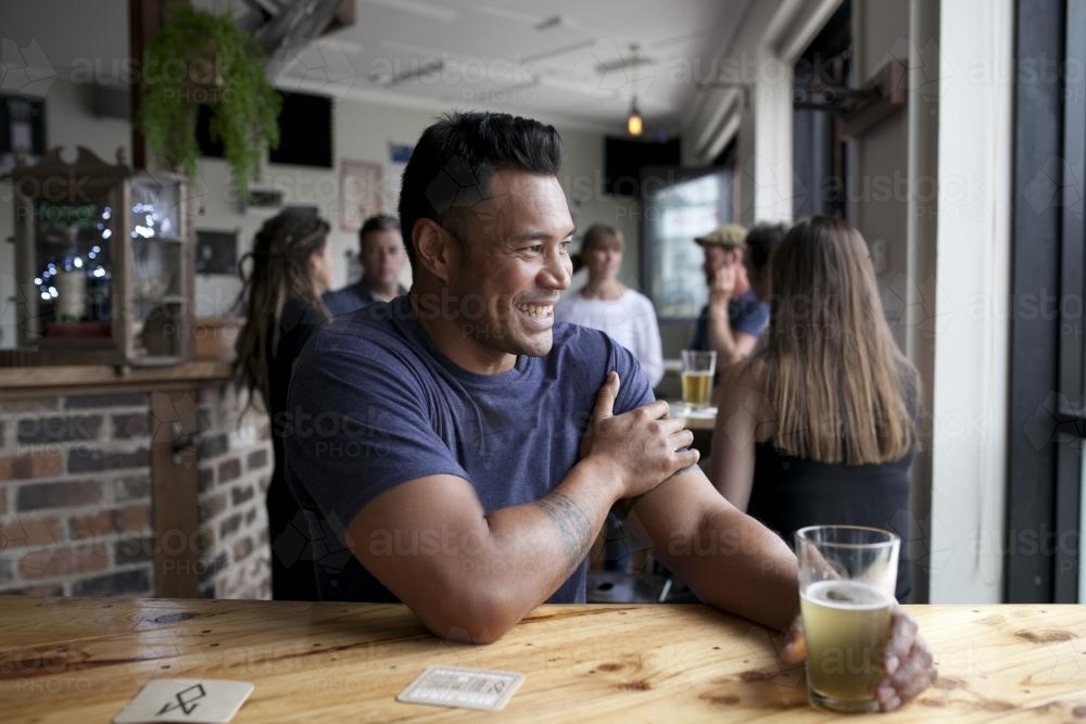 Laughing Polynesian man having a drink at local pub - Australian Stock Image