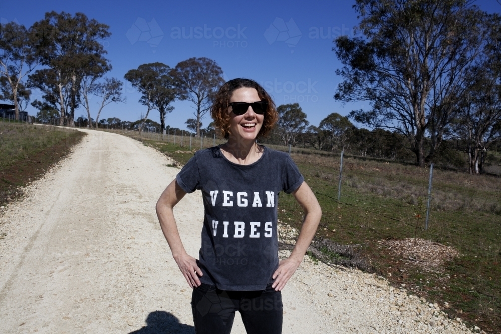 Laughing woman wearing vegan slogan t-shirt standing on rural dirt road - Australian Stock Image
