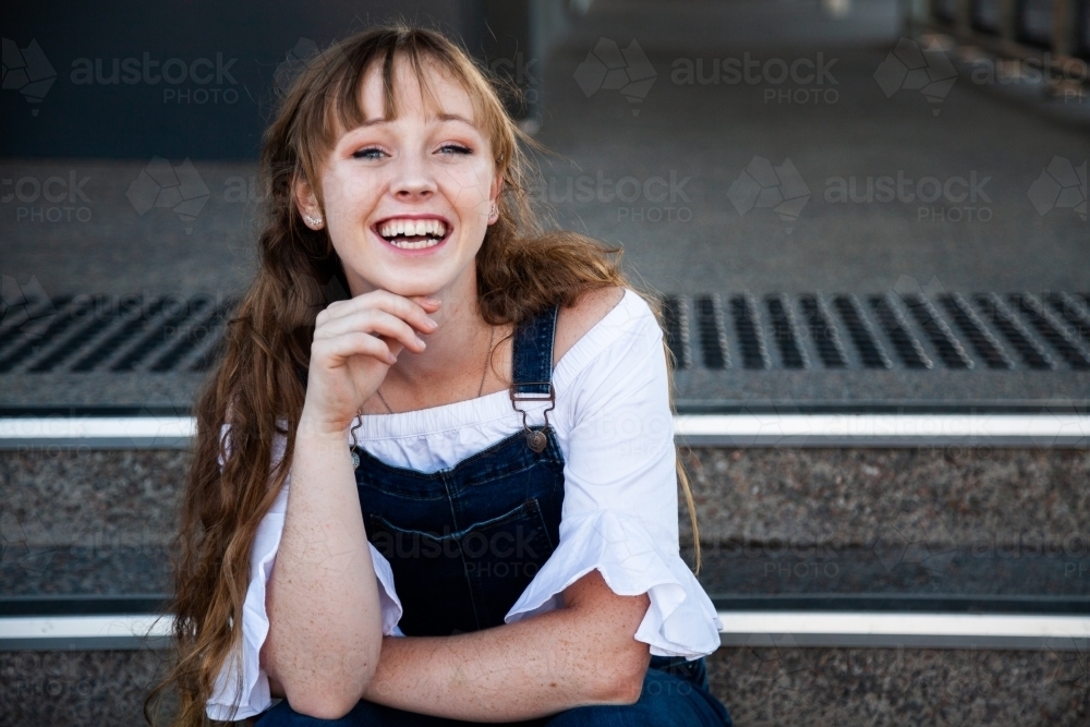 Laughing young adult sitting on steps - Australian Stock Image