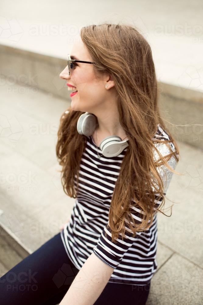 Laughing young woman looking away over shoulder with headphones - Australian Stock Image