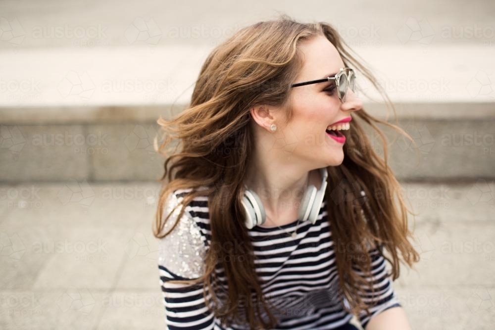 Laughing young woman looking over shoulder with headphones - Australian Stock Image