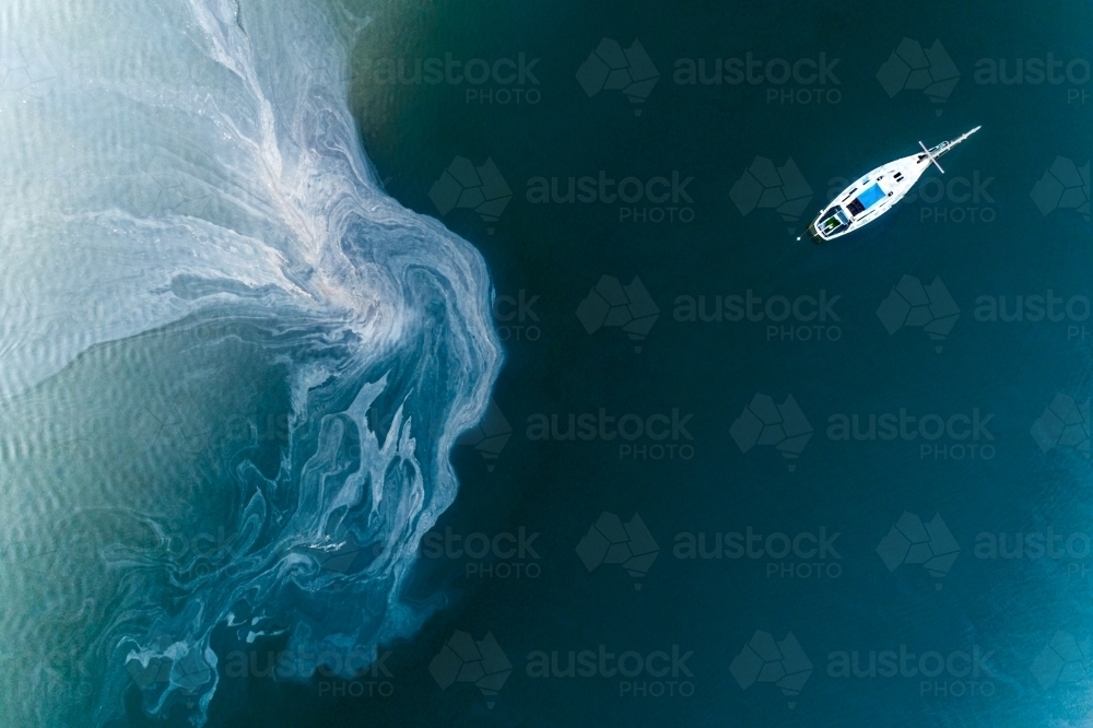 Leachate flowing off tidal mud flats near an anchored yacht. - Australian Stock Image