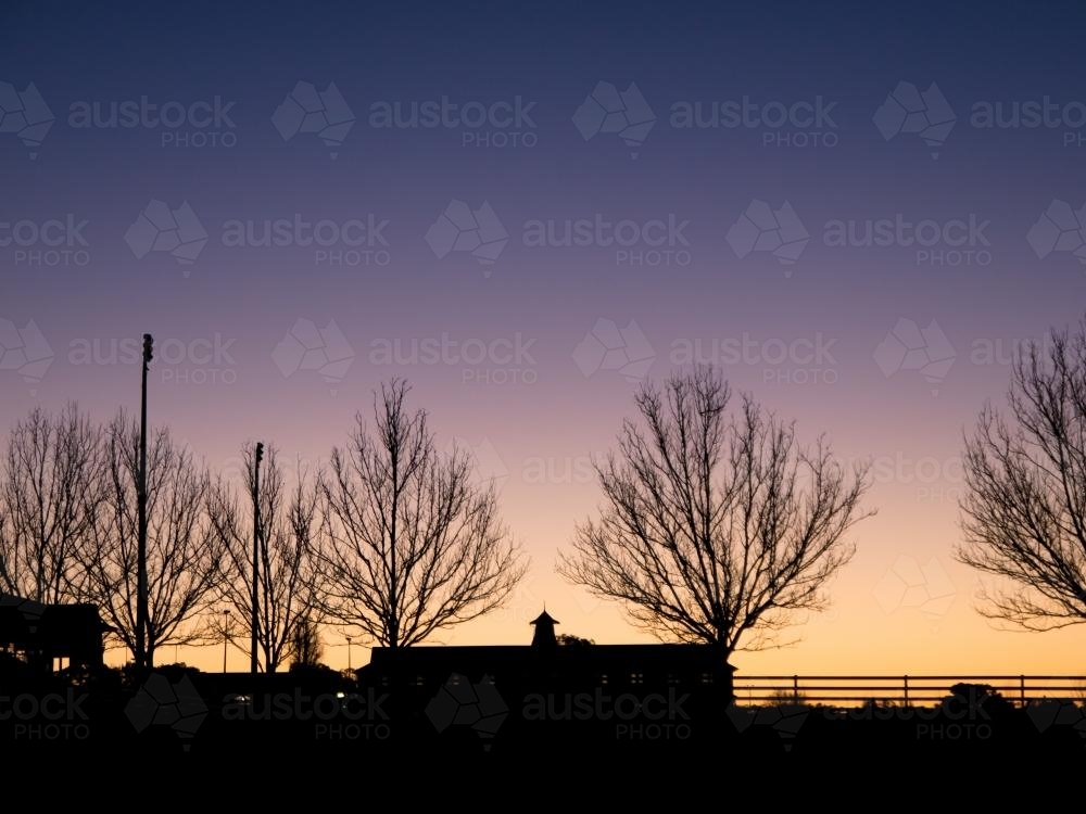 Leafless trees and house silhouetted against sky at sunrise - Australian Stock Image