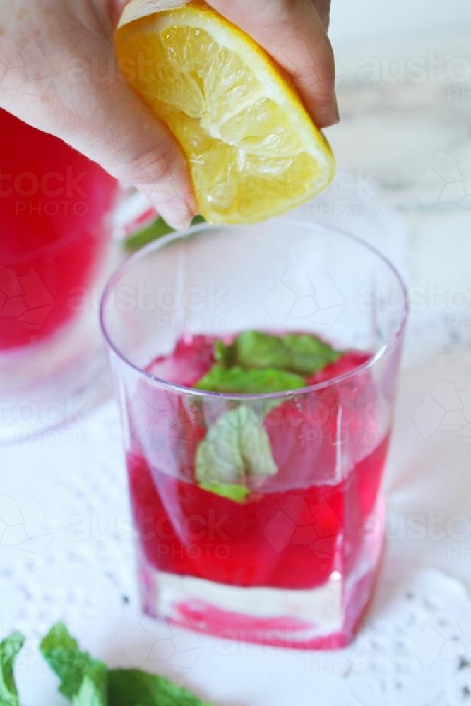 Lemon Squeeze into a glass with red drink with mint - Australian Stock Image
