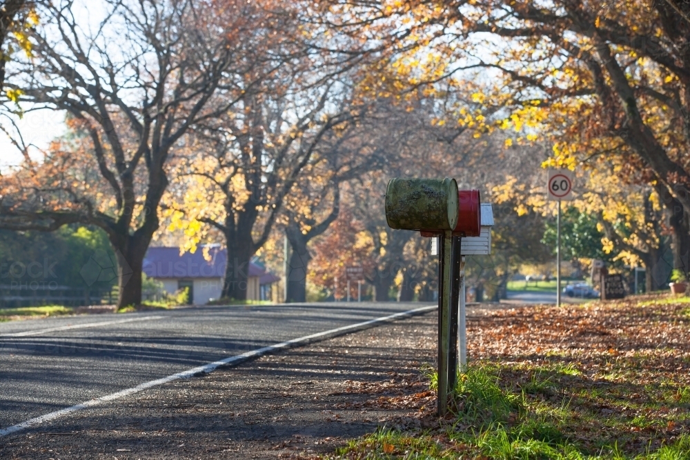 Letterboxes lined up on tree lined road through country town - Australian Stock Image