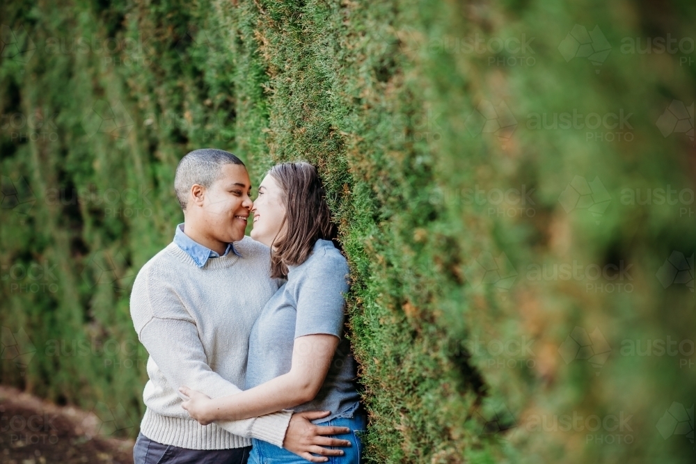 Lgbtqi couple hugging each other and looking at each others faces while leaning on a wall with moss - Australian Stock Image