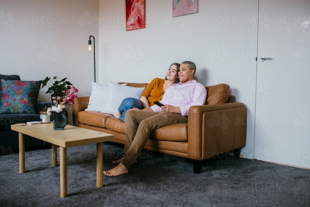 lgbtqi couple sitting on a brown leather couch - Australian Stock Image