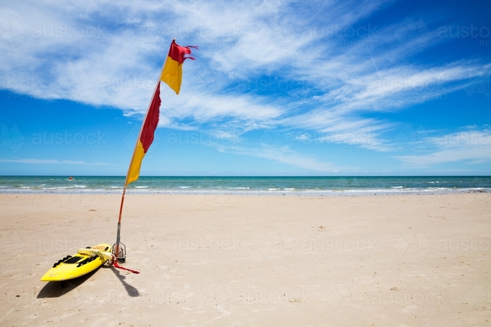 Life saver board and flag on sandy beach - Australian Stock Image