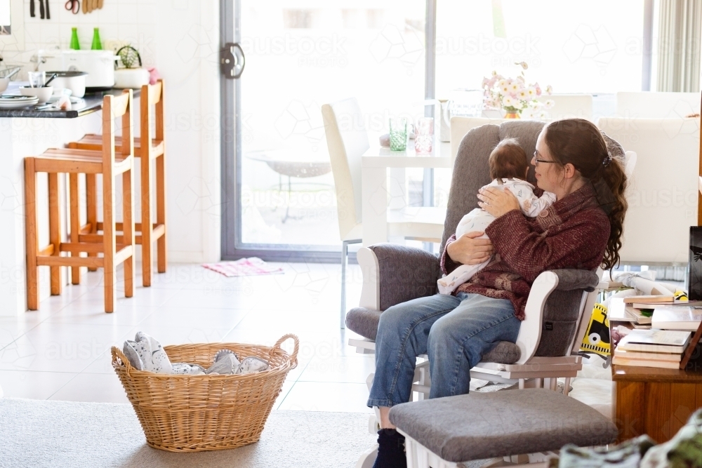 lifestyle image of mother comforting newborn baby to sleep in rocking chair - Australian Stock Image