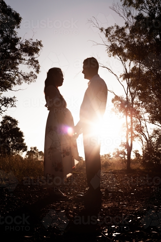 Light flare behind silhouetted pregnant couple in nature - Australian Stock Image