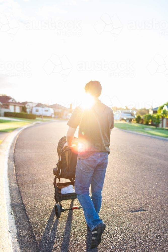 Light Flare over parent pushing pram down quiet street - Australian Stock Image