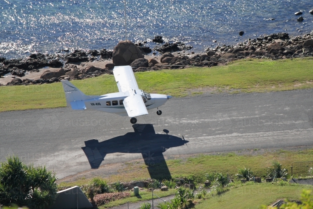 Light plane coming in for landing on coastal Keswick Island - Australian Stock Image