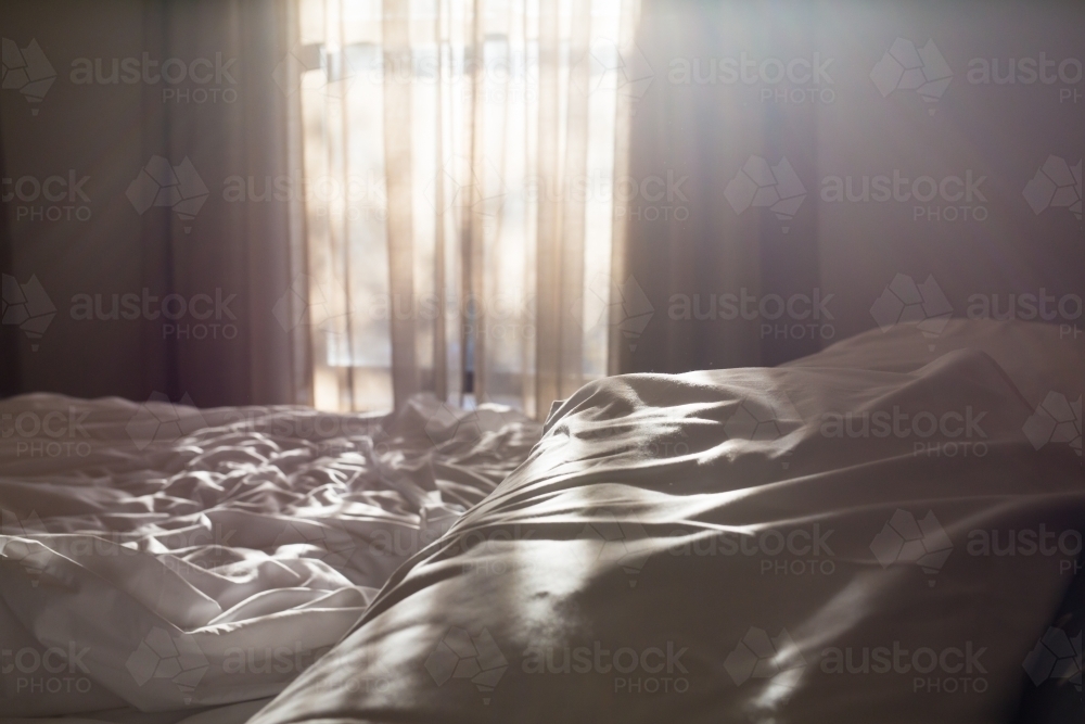 Light through a bedroom window onto a unmade bed - Australian Stock Image