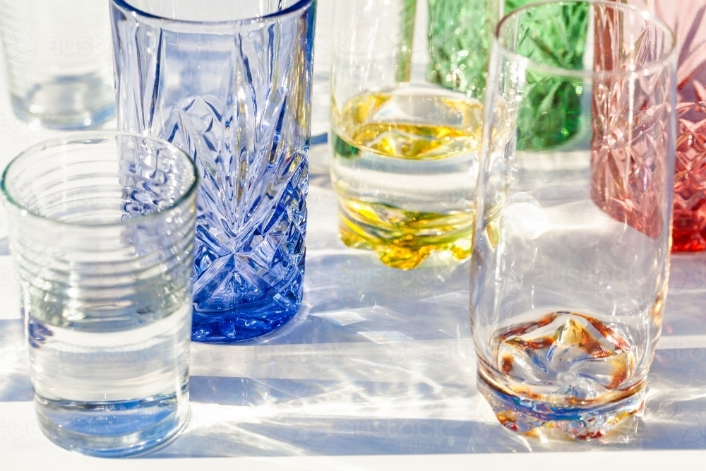 Light through collection of colourful water glasses in sunlight - Australian Stock Image