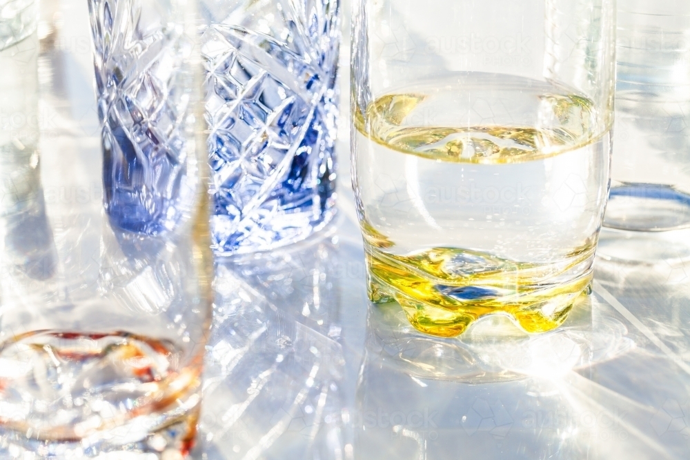 Light through collection of colourful water glasses in sunlight - Australian Stock Image